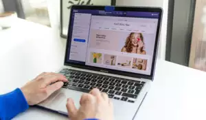 Des mains tapant sur un ordinateur portable affichant un site web d&eacute;di&eacute; &agrave; la beaut&eacute;, avec des photos de produits de soin et une femme souriante. Une ambiance lumineuse et accueillante.
