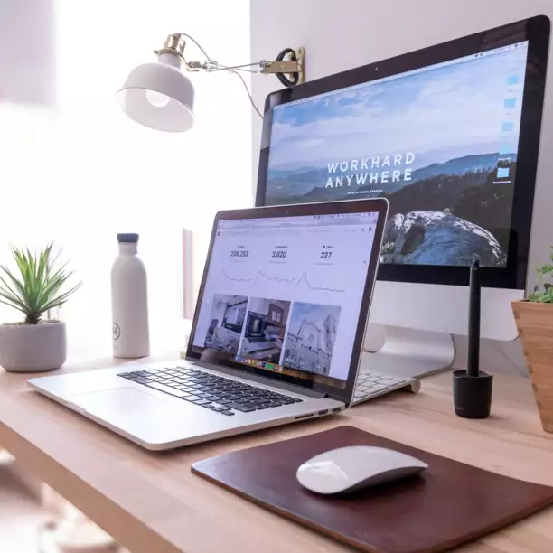 Un bureau moderne &eacute;quip&eacute; d'un ordinateur portable et d'un &eacute;cran offrant une vue panoramique. Une petite plante, une bouteille d'eau et une souris sont dispos&eacute;es &agrave; proximit&eacute;, cr&eacute;ant ainsi un espace de travail bien rang&eacute;.