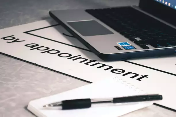 Gros plan sur un ordinateur portable posé sur un panneau indiquant « sur rendez-vous », avec un bloc-notes et un stylo au premier plan. La scène dégage une impression de professionnalisme et d'organisation.