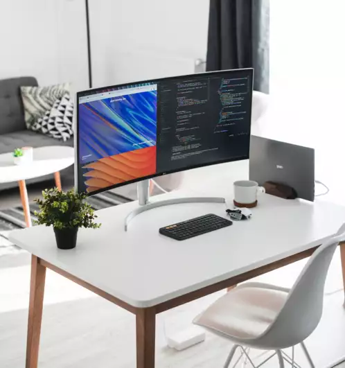 Un bureau &agrave; domicile moderne avec un bureau blanc &eacute;pur&eacute;, un grand &eacute;cran affichant des graphiques color&eacute;s et du code, une petite plante, un clavier et une tasse. Une ambiance chaleureuse et &eacute;l&eacute;gante.