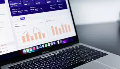 Ordinateur portable ouvert affichant un tableau de bord financier avec des graphiques et des statistiques. L'&eacute;cran pr&eacute;sente des diagrammes &agrave; barres et des donn&eacute;es chiffr&eacute;es, sugg&eacute;rant une analyse de donn&eacute;es.