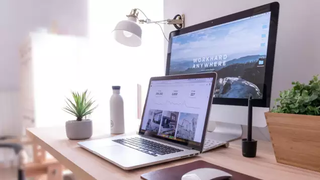 Un bureau moderne &eacute;quip&eacute; d'un ordinateur portable et d'un &eacute;cran offrant une vue panoramique. Une petite plante, une bouteille d'eau et une souris sont dispos&eacute;es &agrave; proximit&eacute;, cr&eacute;ant ainsi un espace de travail bien rang&eacute;.